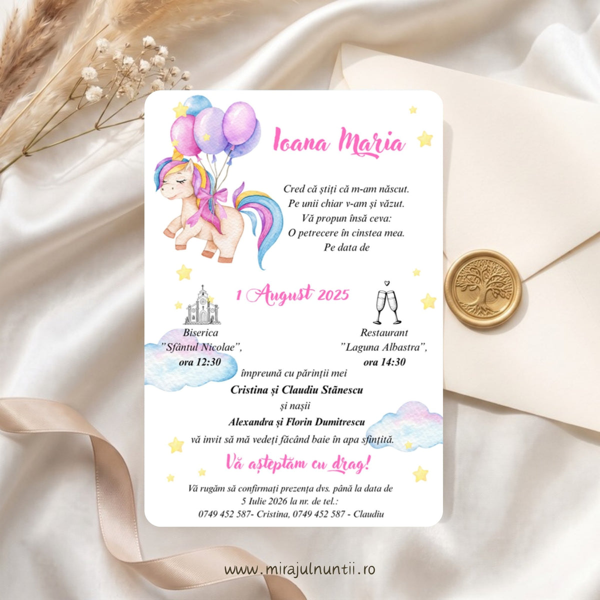 Invitație de botez tipărită cod Magnific B.15-20015, cu unicorn în acuarelă cu coamă curcubeu care ține baloane roz și lila, numele Ioana Maria scris caligrafic cu roz, nori pastel și steluțe galbene, lângă un plic crem cu sigiliu auriu din ceară