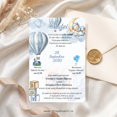 Invitație de botez cu ursuleț care doarme pe lună, baloane cu aer cald în dungi bleu, nori în acuarelă și cuburi BOY, numele Matei scris caligrafic, lângă un plic crem cu sigiliu auriu, cod Magnific B.20-20020