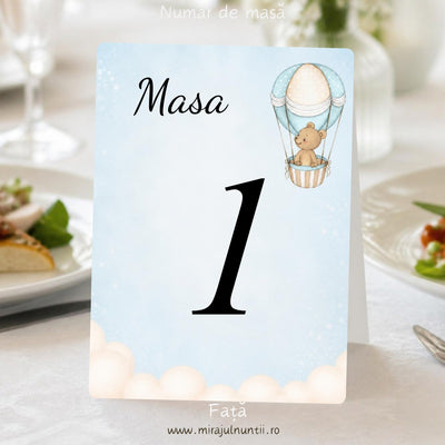 Număr de masă botez „Masa 1”, fața, cu ursuleț în balon cu aer cald în dreapta sus și nori pufoși jos, pe cer bleu pal în acuarelă, carton alb satinat – cod Magnific B.3-20003