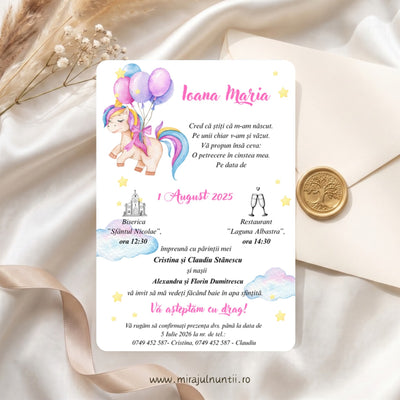 Invitație de botez tipărită cod Magnific B.15-20015, cu unicorn în acuarelă cu coamă curcubeu care ține baloane roz și lila, numele Ioana Maria scris caligrafic cu roz, nori pastel și steluțe galbene, lângă un plic crem cu sigiliu auriu din ceară