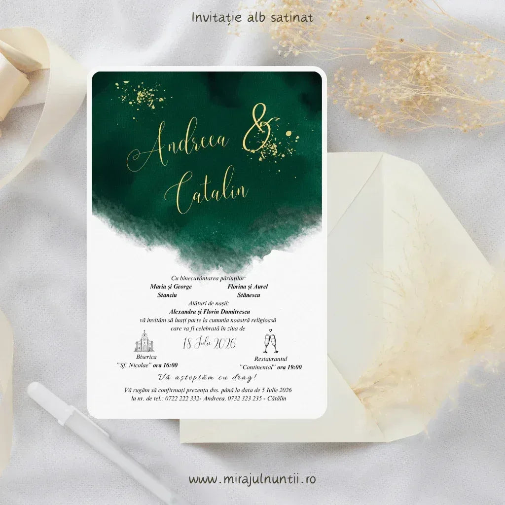 Invitație de nuntă cod Magnific C.1 pe carton alb satinat, cu acuarelă verde-smarald în partea de sus, nume aurii scrise caligrafic și accente aurii, lângă un plic alb și ierburi pampas.