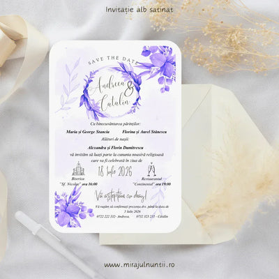 Invitație de nuntă cod Magnific C.31 pe carton alb satinat, cu flori violet în acuarelă și coroniță de frunze mov în jurul numelor, lângă un plic crem.