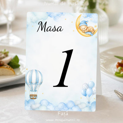 Număr de masă botez „Masa 1”, fața, cu ursuleț care doarme pe lună, balon cu aer cald și baloane bleu printre nori, pe carton alb satinat – cod B.20-20020