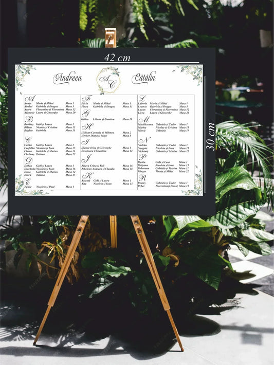 Opis nuntă orizontal 42 x 30 cm cod Miraj 5048 pe șevalet, cu numele mirilor scrise caligrafic, monogramă în hexagon auriu, frunze verzi în acuarelă și lista invitaților pe mese.